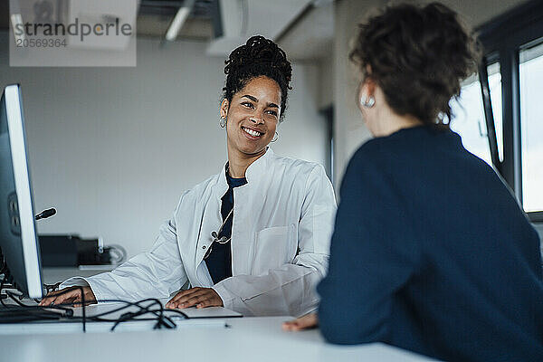 Smiling doctor discussing with patient at desk in hospital