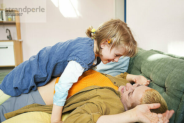 Playful girl leaning on mother lying on sofa at home