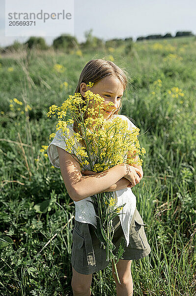 Smiling girl holding bunch of flowers and standing in farm