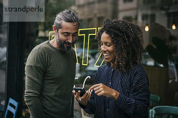 Happy friends sharing smartphone standing near shop