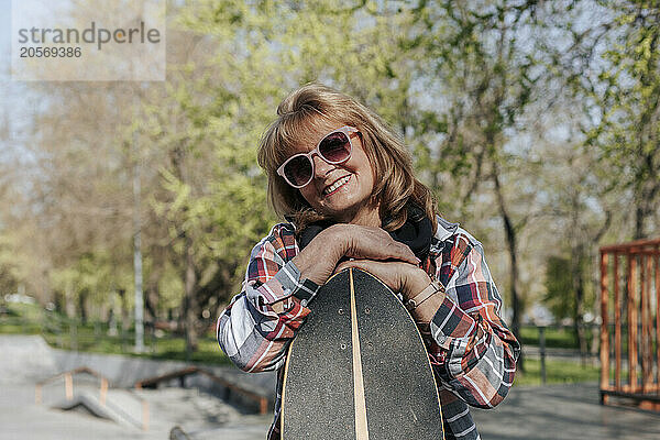 Smiling senior woman standing with skateboard at park