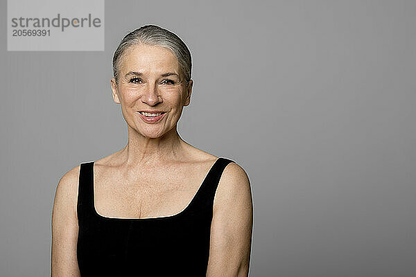 Smiling senior woman in black sports clothing against gray background