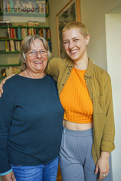 Smiling woman in casuals standing with senior mother at home