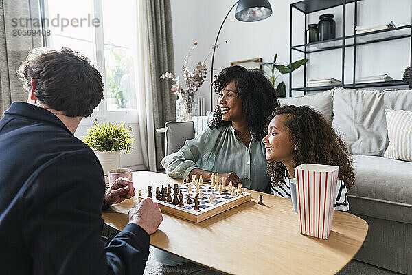 Parents sitting in livingroom teaching daughter to play chess