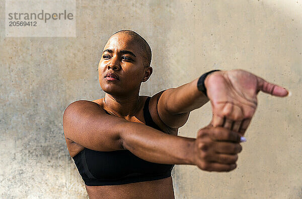 Confident woman in sportswear doing warm up exercise in front of wall