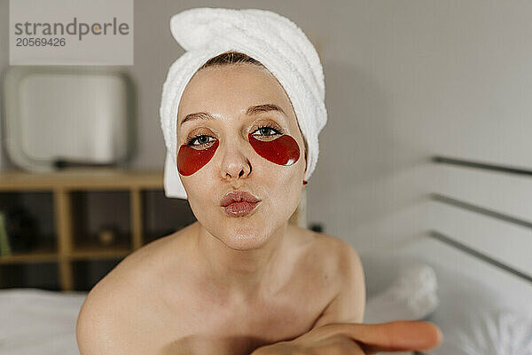 Woman with eye patches and towel making puckering face at home