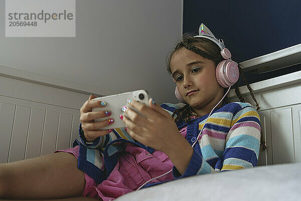 Girl listening music through headphones using mobile phone at home