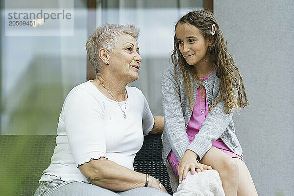 Happy grandmother talking with cute granddaughter at patio