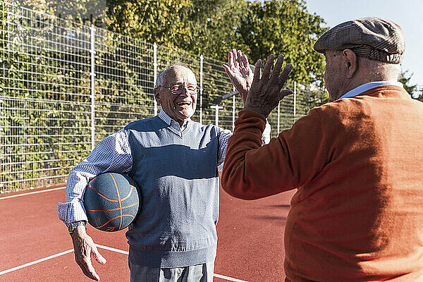 Happy friends playing and giving high five at basketball court