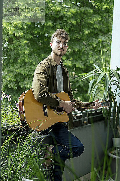 Confident young man with acoustic guitar standing in balcony