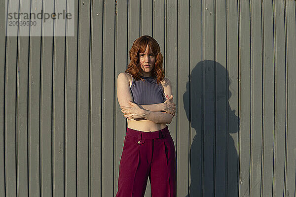 Confident redhead woman with arms crossed standing in front of gray wall