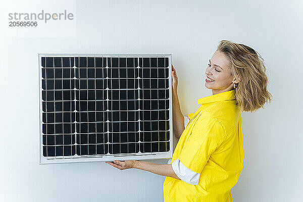 Smiling freelancer holding solar panel near wall