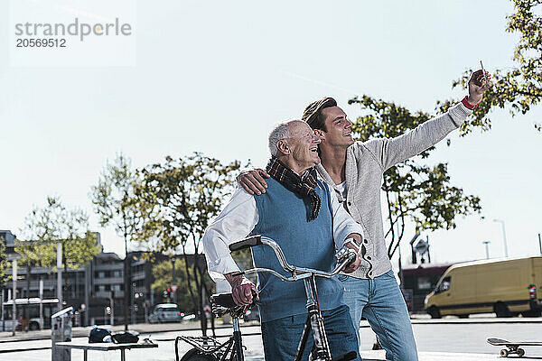 Happy young man photographing through smart phone with grandfather at street