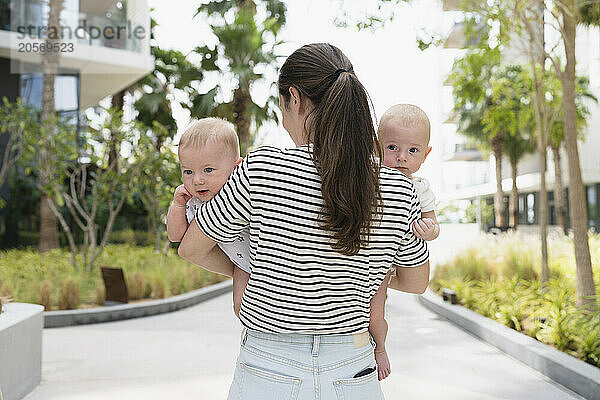 Mother with ponytail carrying twin sons in back yard