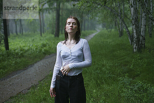 Woman with eyes closed standing in rain at forest