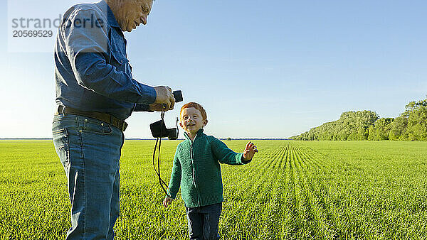 Grandfather shows his grandson old camera in field.