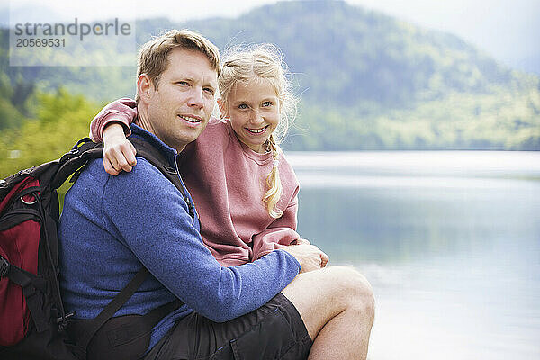 Happy man sitting with daughter near lake