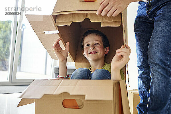 Smiling boy sitting in cardboard box next to father at new apartment