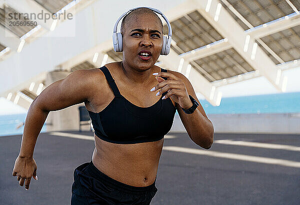 Athletic woman wearing wireless headphones running on road in Spain