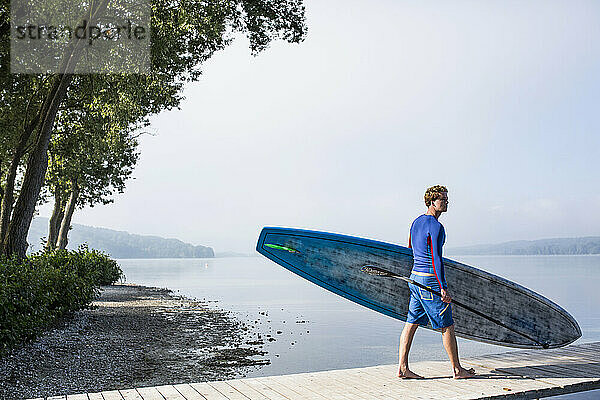 Young man carrying paddleboard and oar on sunny day