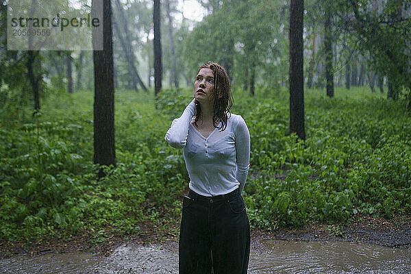 Beautiful woman with hand in hair standing in rain at forest