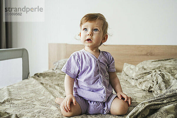 Cute baby kneeling on bed at home