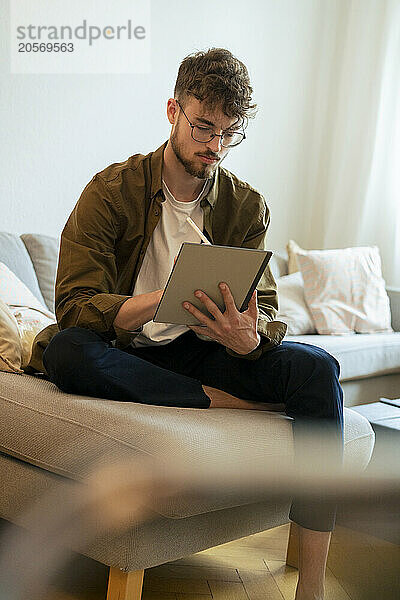 Handsome young man using tablet PC sitting on sofa at home