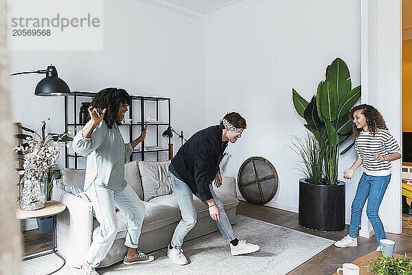 Happy parents playing blind man's buff with their daughter in the living room