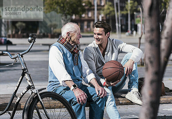 Happy young man holding basketball and talking to grandfather on sunny day