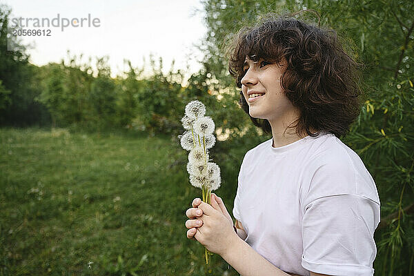 Smiling girl with bunch of dandelions near green plants