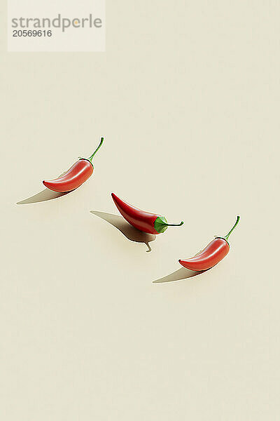 Three red chili peppers on beige background