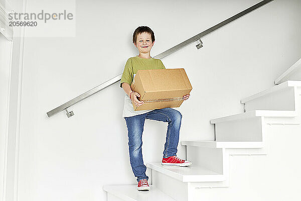 Smiling boy standing with box on staircase of new house