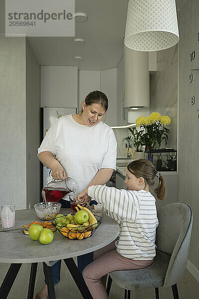 Woman serving juice to daughter sitting at dining table