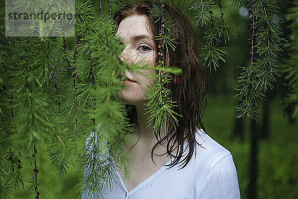 Woman peeking through green leaves in forest