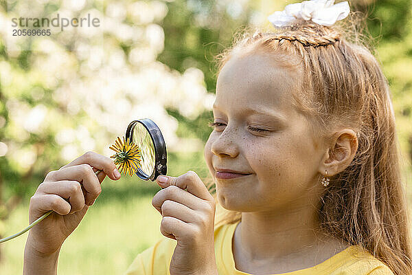 Girl looking at flower through magnifying glass in garden