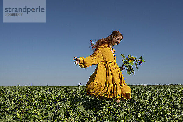 Teenage girl with red hair in a yellow dress running with sunflowers in a green field