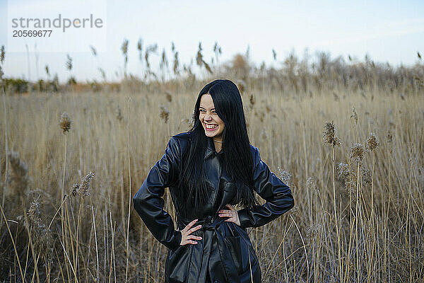 Smiling young woman standing with hands on hip in reeds at field