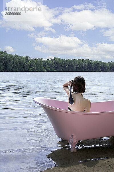 Girl bathing inside pink bathtub under cloudy sky in lake