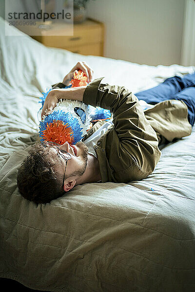 Young man hugging rocketship shaped pinata lying on bed at home