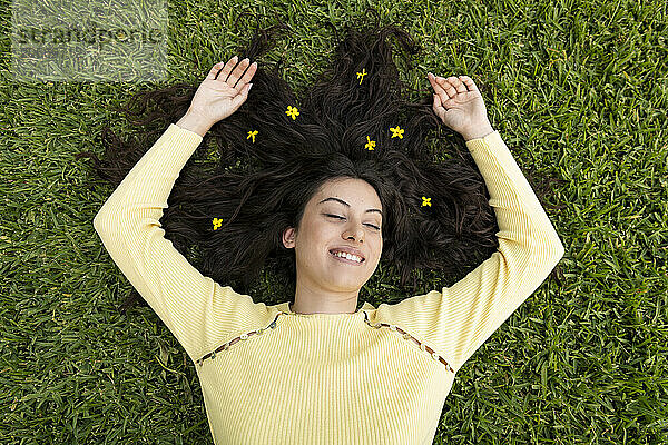 Happy woman with arms raised lying on grass at garden