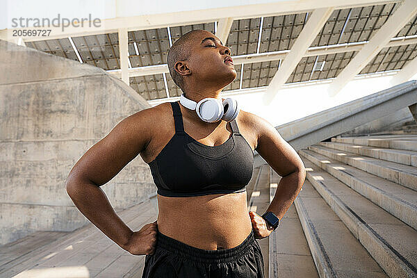 Confident sporty woman standing with arms akimbo on stairs