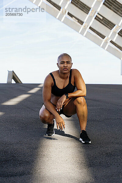 Confident sporty woman crouching on road