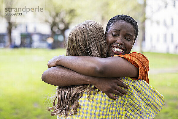 Smiling woman with eyes closed hugging young friend at park