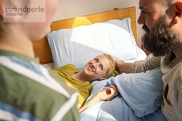 Smiling woman looking at family lying on bed at home