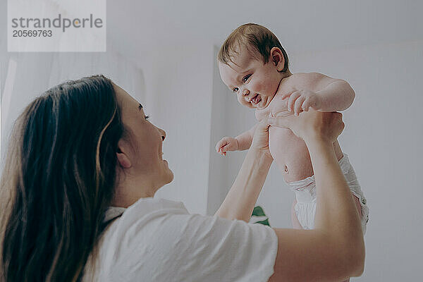 Happy mother holding baby aloft at home