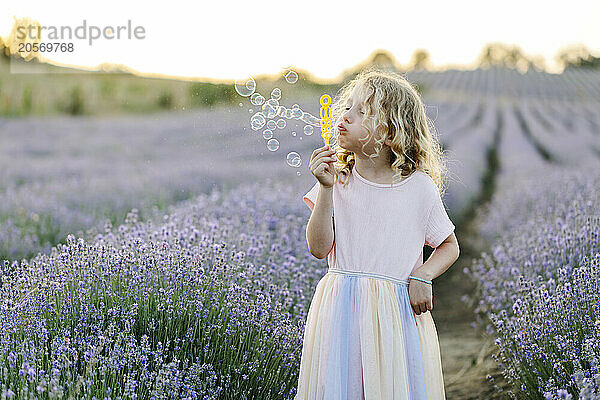 Blond hair girl blowing bubbles and standing in lavender field