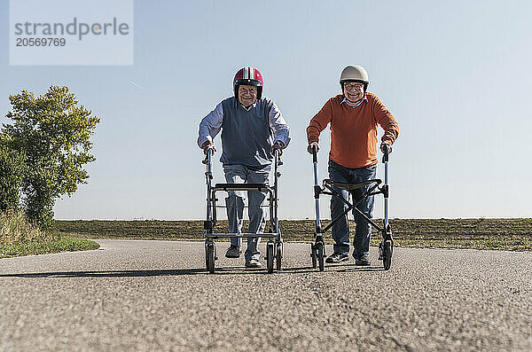 Senior friends wearing safety helmets competing for wheeled walker race