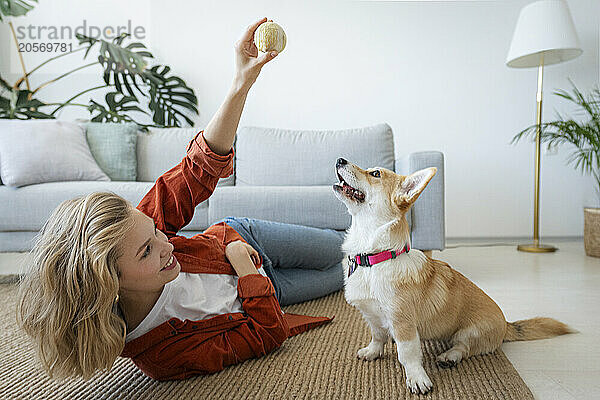 Woman holding ball lying down near dog at home