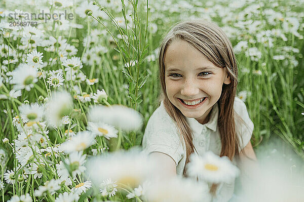 Happy girl looking at daisy flower in field