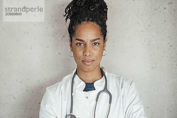 Confident young female doctor in front of gray wall at hospital